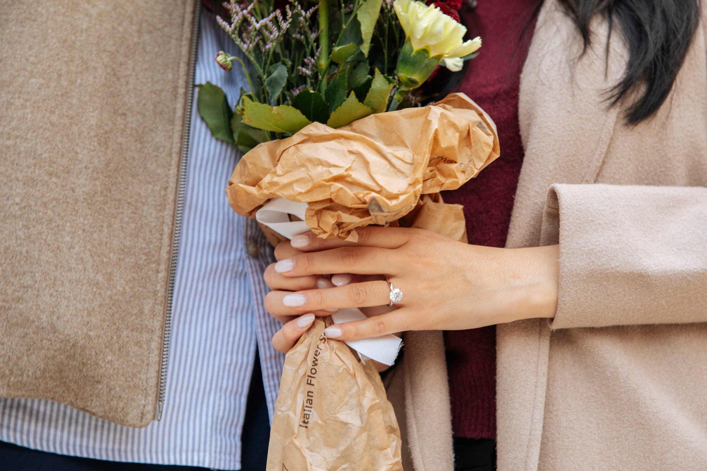 Kelly's hand with her engagement ring, holding a bouquet wrapped in paper